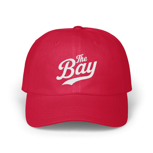 Red baseball cap with "The Bay" embroidered in white script.