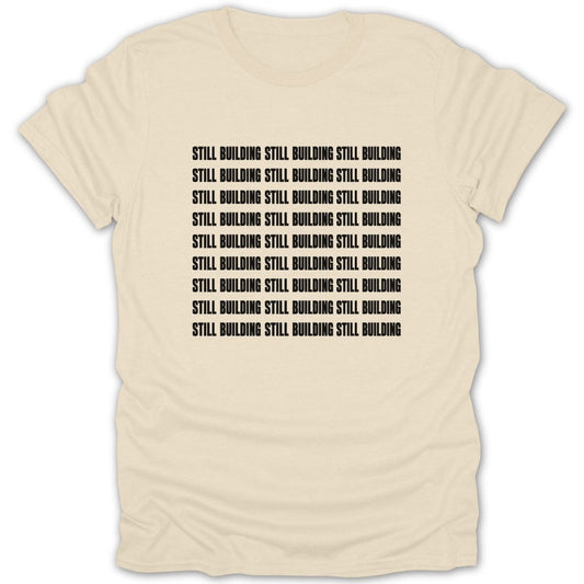 Cream t-shirt with repeated black text "STILL BUILDING".