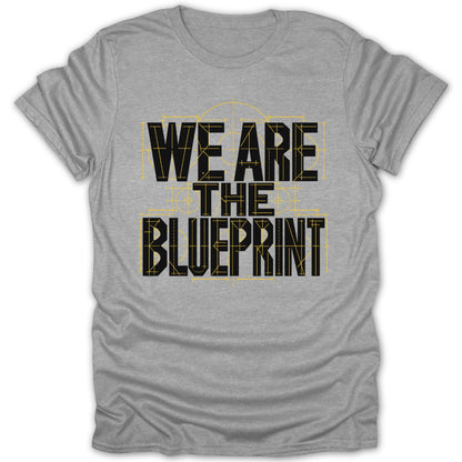 Grey t-shirt with black text "WE ARE THE BLUEPRINT" over yellow blueprint lines.