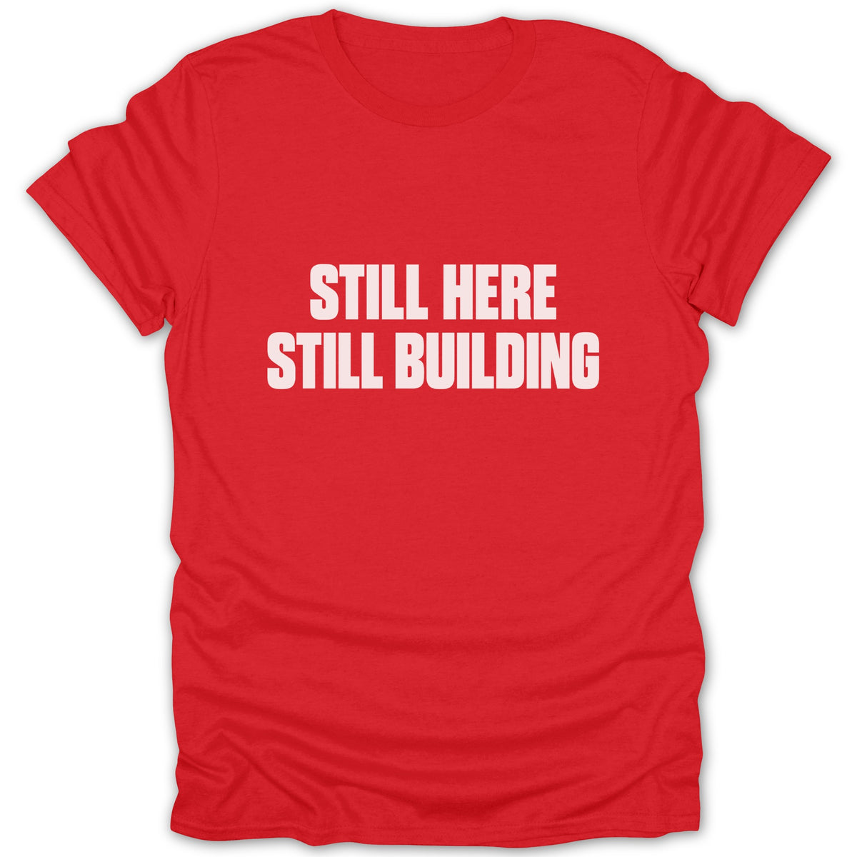 A red short-sleeved t-shirt with white text reading "STILL HERE STILL BUILDING" centered on the chest.