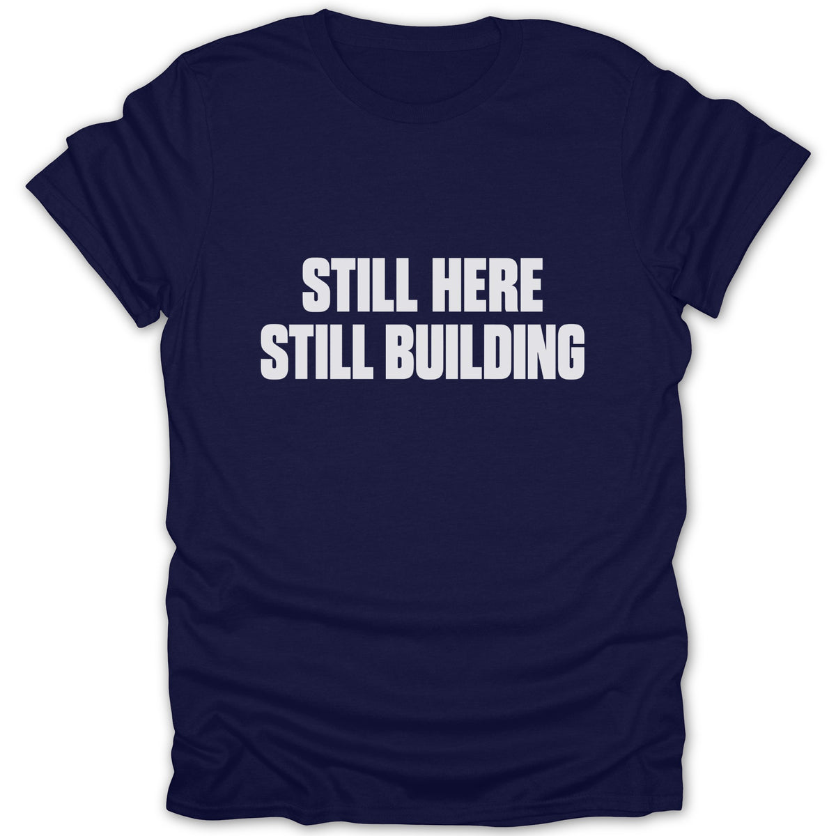 Navy blue short-sleeved t-shirt with white block text reading STILL HERE STILL BUILDING on the chest.