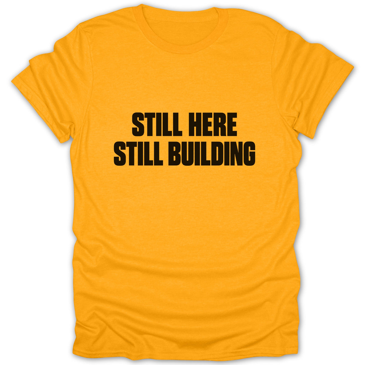 A yellow short-sleeved t-shirt with black text that reads "STILL HERE STILL BUILDING" on the chest.