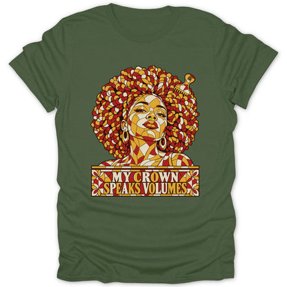An olive green t-shirt featuring a stained glass-style graphic of a Black woman with a large afro and pick comb, with text reading MY CROWN SPEAKS VOLUMES.