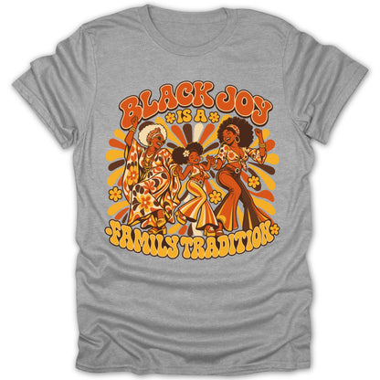 Three women dance on a t-shirt with text "BLACK JOY IS A FAMILY TRADITION".