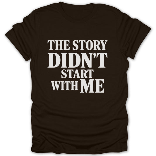 A dark brown short-sleeved t-shirt featuring white text that reads "THE STORY DIDN'T START WITH ME".