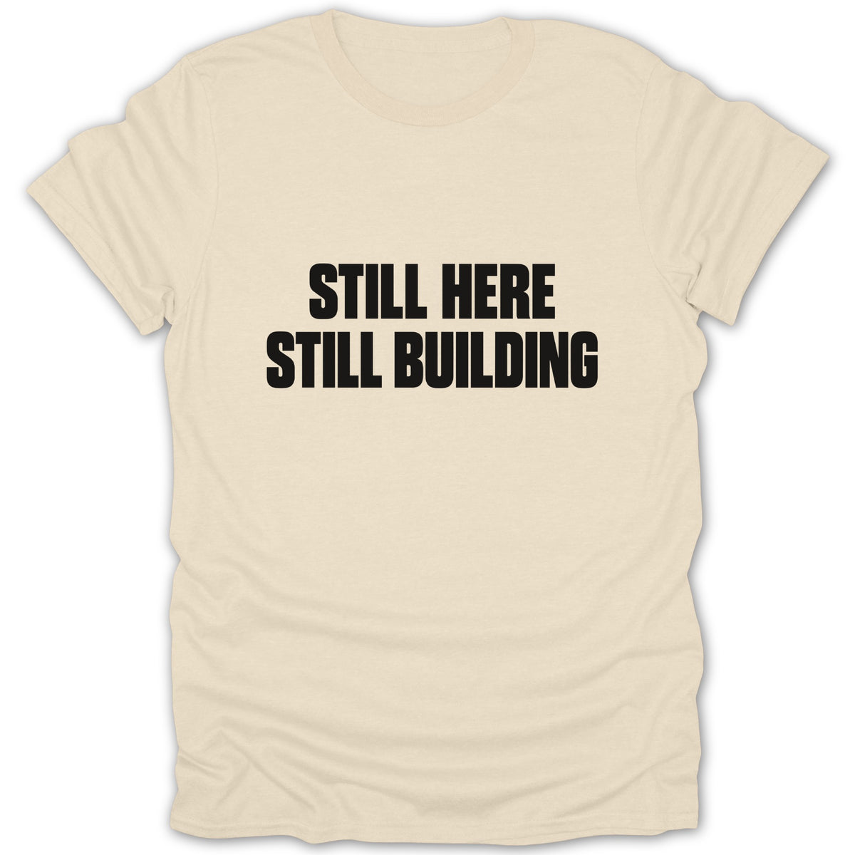 Cream crewneck t-shirt with black text on the chest that reads "STILL HERE STILL BUILDING."