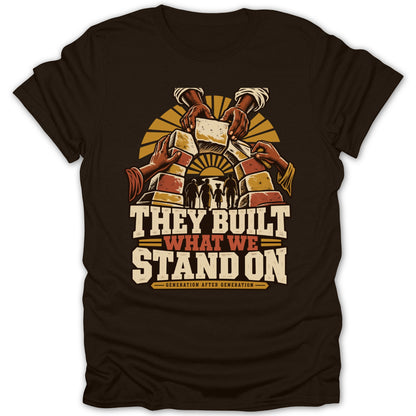 Brown t-shirt with graphic: hands building arch, silhouettes, text "THEY BUILT WHAT WE STAND ON".