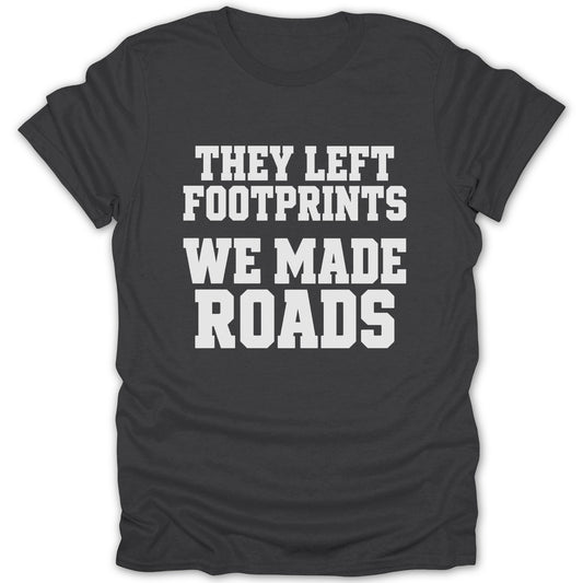 A dark gray crewneck t-shirt with white block lettering that reads THEY LEFT FOOTPRINTS WE MADE ROADS.