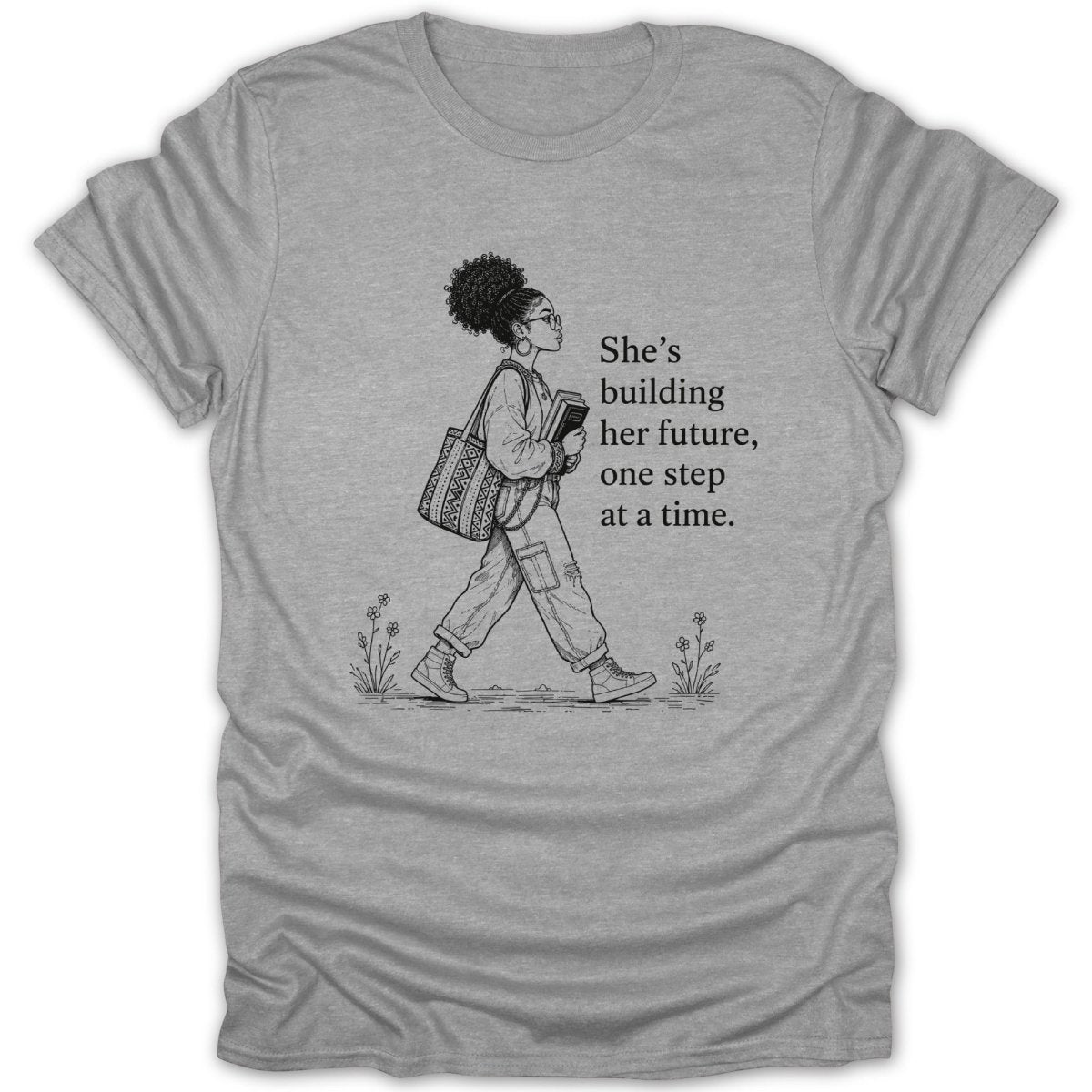 Grey t-shirt with black line art of a woman walking and text "She's building her future, one step at a time."
