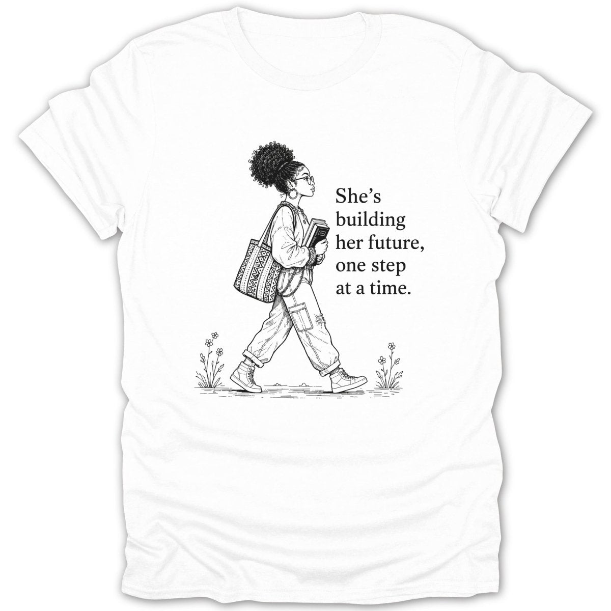 Black and white graphic on white t-shirt of a woman carrying books, with text "She's building her future, one step at a time."