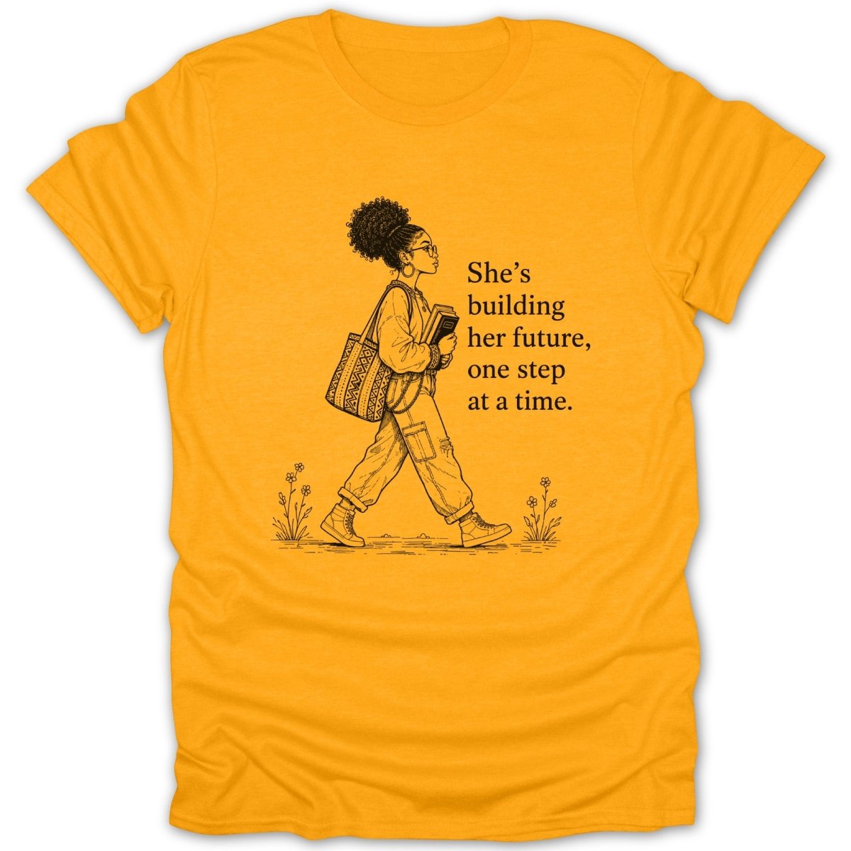 Yellow t-shirt with drawing of woman walking, holding books, and text "She's building her future, one step at a time."