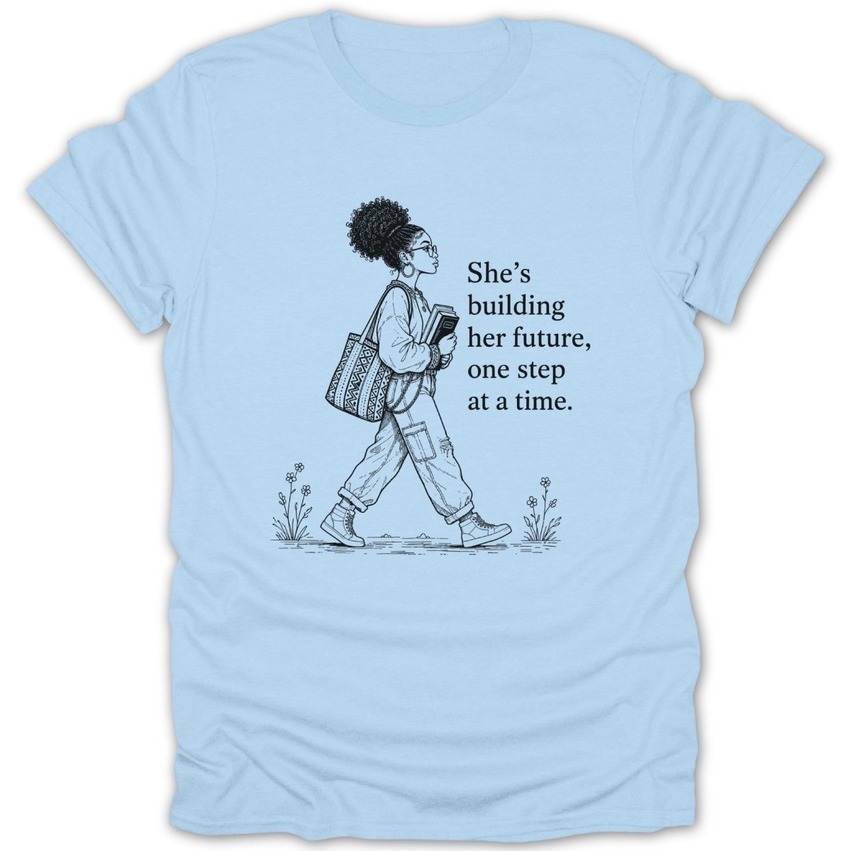 Light blue t-shirt with a sketch of a woman walking and text "She's building her future, one step at a time."