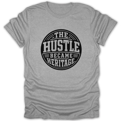 Grey t-shirt with a black circular graphic reading "The Hustle Became Heritage".