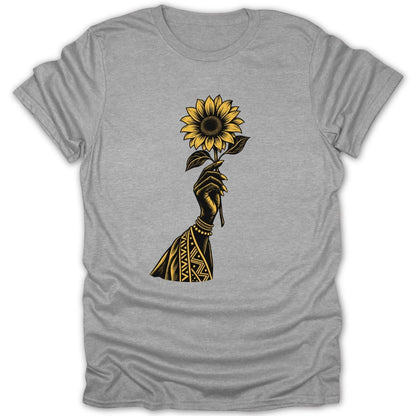 Black hand with geometric patterns holding a yellow sunflower on a grey t-shirt.