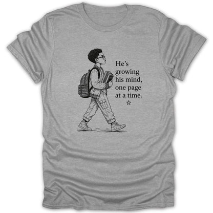 Grey t-shirt with a sketch of a boy walking and the text "He's growing his mind, one page at a time."